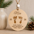 Personalized baby's first Christmas ornament featuring engraved baby footprints, a custom name, birth year, and the message "Our family has grown by two feet!" handcrafted from Baltic birch.