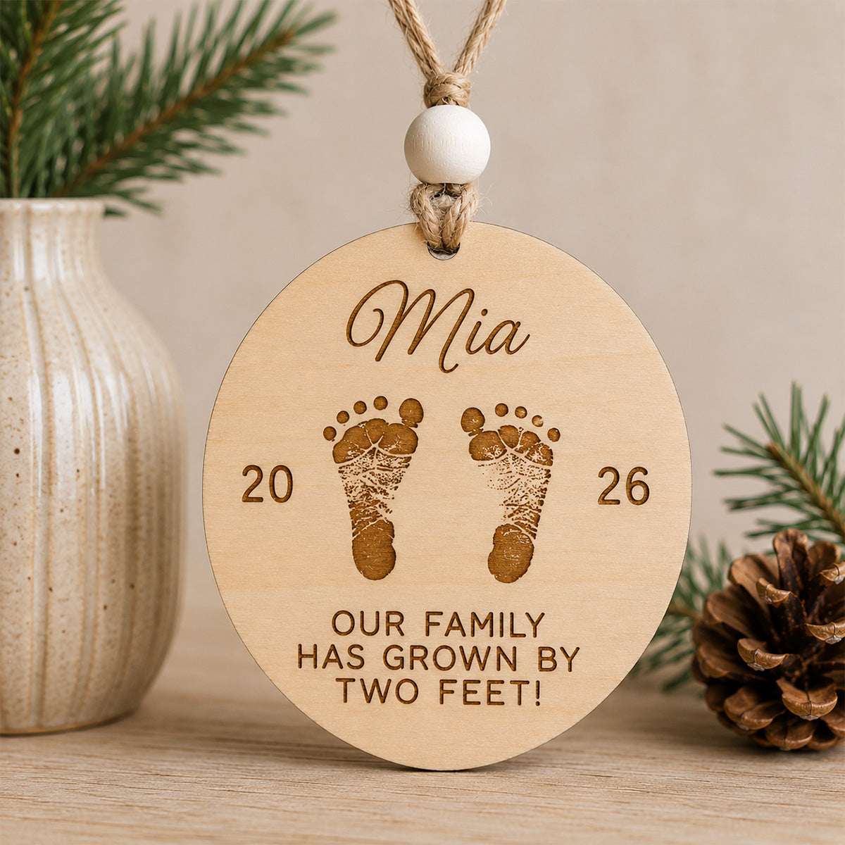 Personalized baby's first Christmas ornament featuring engraved baby footprints, a custom name, birth year, and the message "Our family has grown by two feet!" handcrafted from Baltic birch.