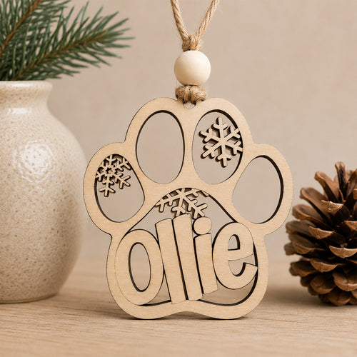 Personalized wooden dog paw Christmas ornament engraved with a pet's name and snowflake accents, handcrafted from Baltic birch.